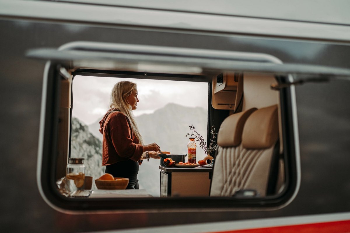 Blick auf eine kochende Frau im Bürstner Wohnmobil durch ein offenes Fenster