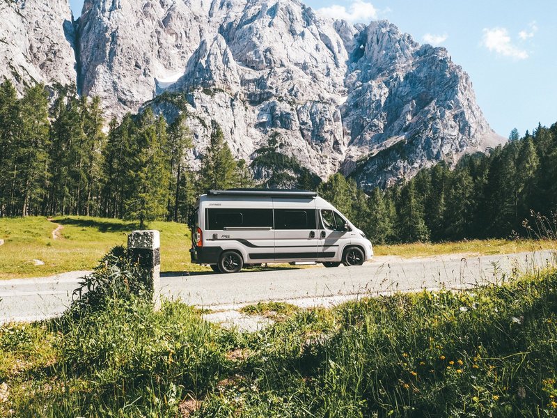 Hymer Camper Van steht an einer Straße, Berge und Wald im Hintergrund