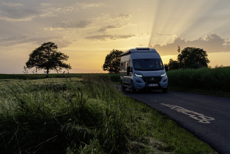 Camper Van fährt in der Dämmerung über eine Straße im Grünen