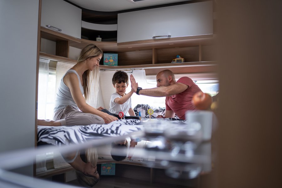 Familie mit Kind spielt auf einem Bett im Bürstner Wohnwagen