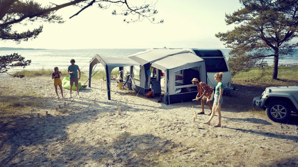 Luftvorzelt vor einem Wohnwagen mit spielenden Personen am Strand 