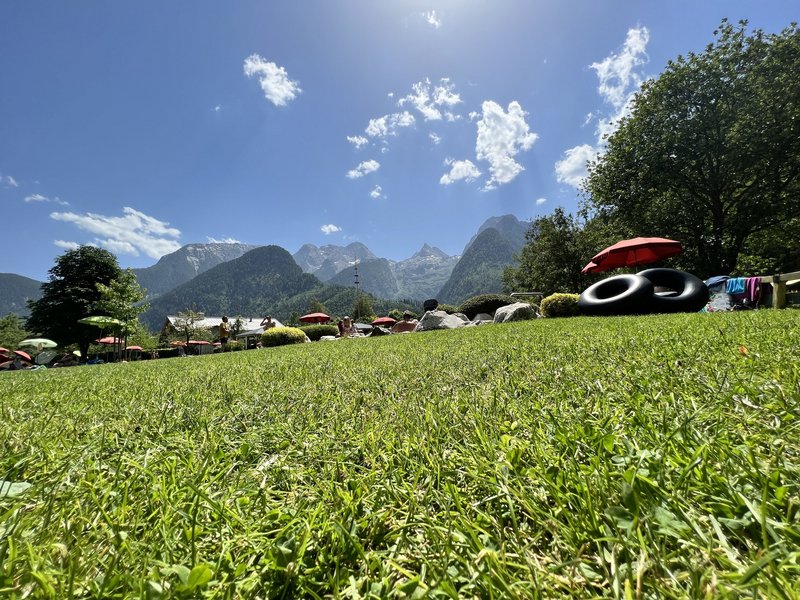 Menschen mit Sonnenschirmen auf einer Wiese vor Berglandschaft