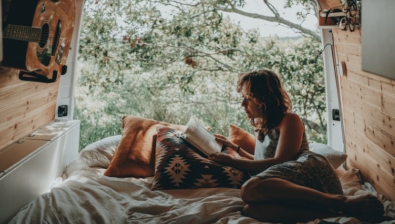 Frau liest Buch im Kofferraum eines Vans in der Natur