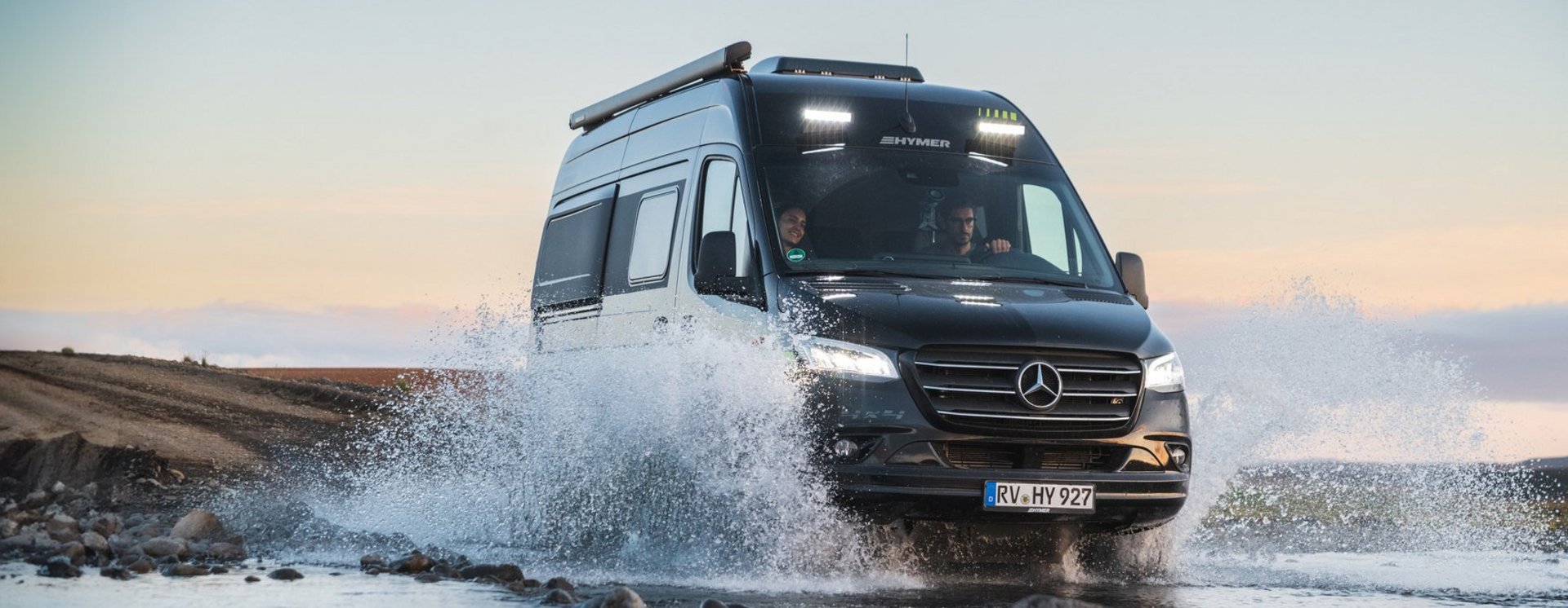 Hymer Camper Van fährt durch seichtes Gewässer, Wasser spritzt nach links und rechts