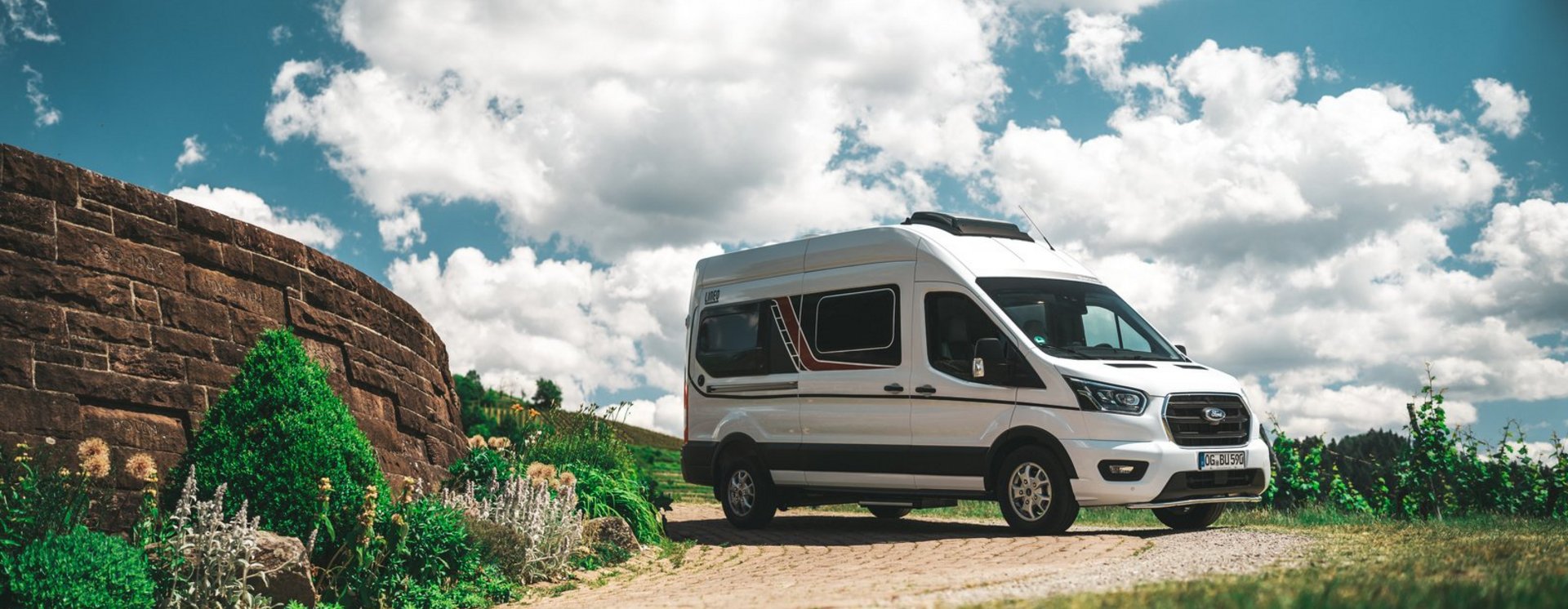 Bürstner Wohnmobil steht im Grünen neben einer Mauer