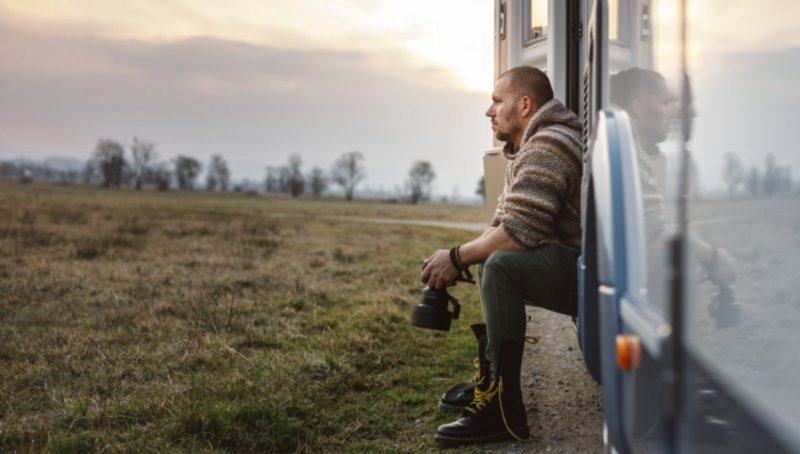 Mann sitzt in der Tür des Campers und blickt in die Natur