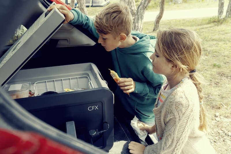 Zwei Kinder mit Eis in der Hand schauen in Kühlbox im Kofferraum