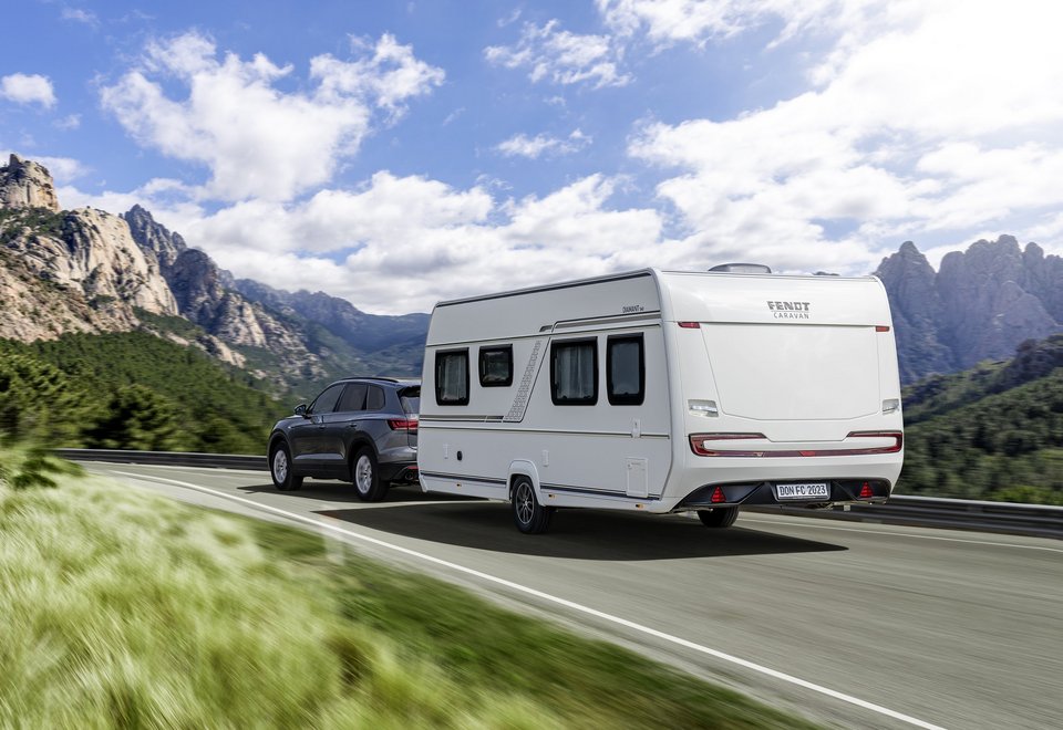 Auto mit Fendt-Caravan auf der Straße im Gebirge 