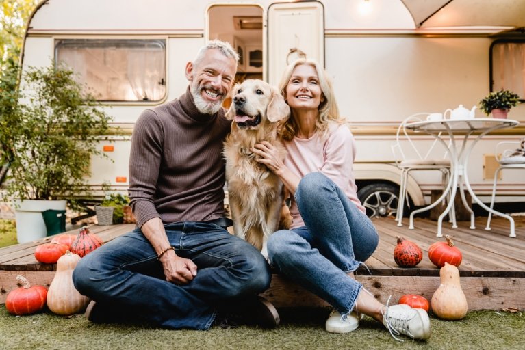 Mann und Frau sitzen mit Hund auf der Terrasse eines Wohnwagens 