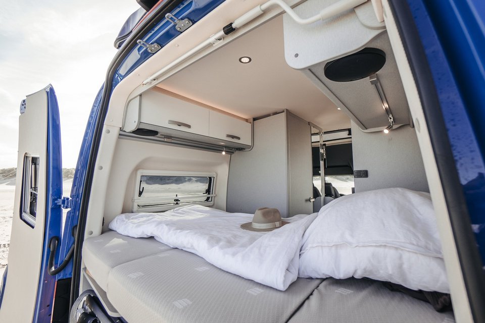 Blick auf Bett eines Camper Vans von außen durch geöffnete Türen