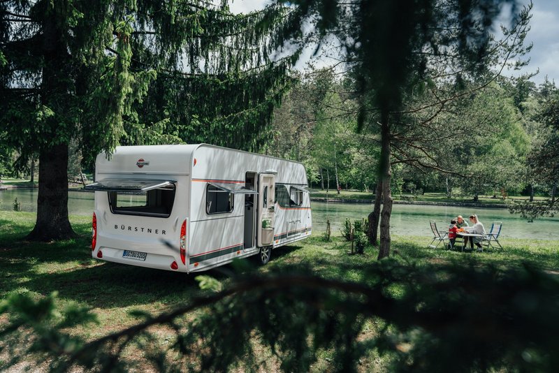 Bürstner Wohnwagen stehend neben einem See, Familie daneben an einem Tisch