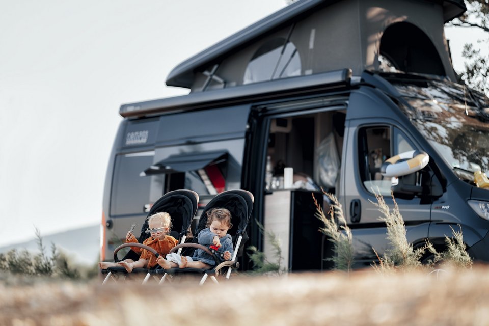 Zwei kleine Kinder sitzen vor einem Camper